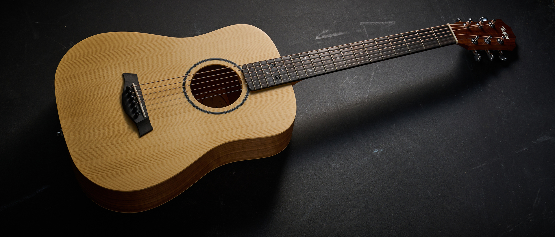 A Taylor BT1e Baby Taylor 3/4 acoustic guitar on a black floor
