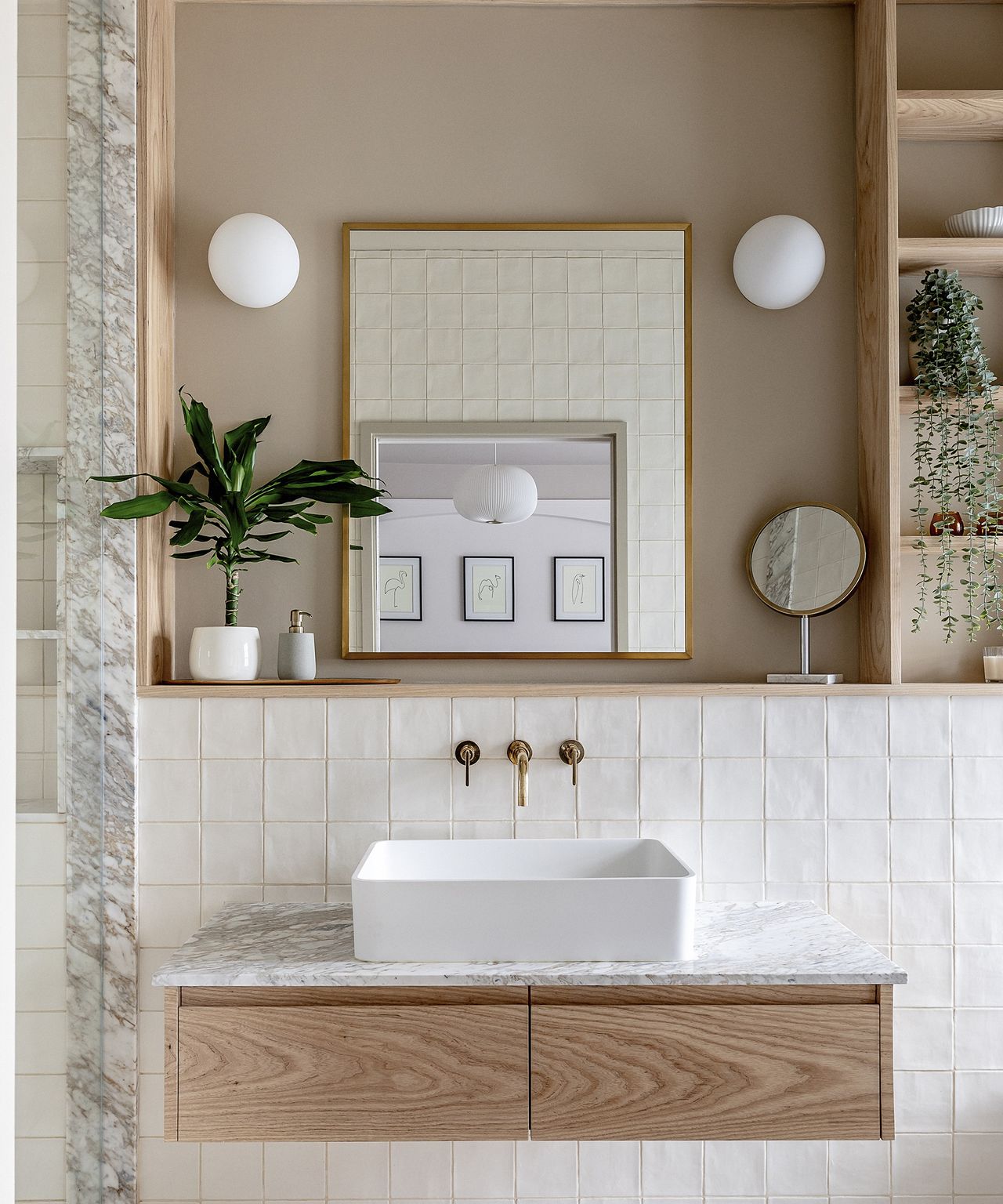 A newly fitted sink in a bathroom with soft brown walls and built in pine wood shelves. The splash back tiles are white and the taps are brass