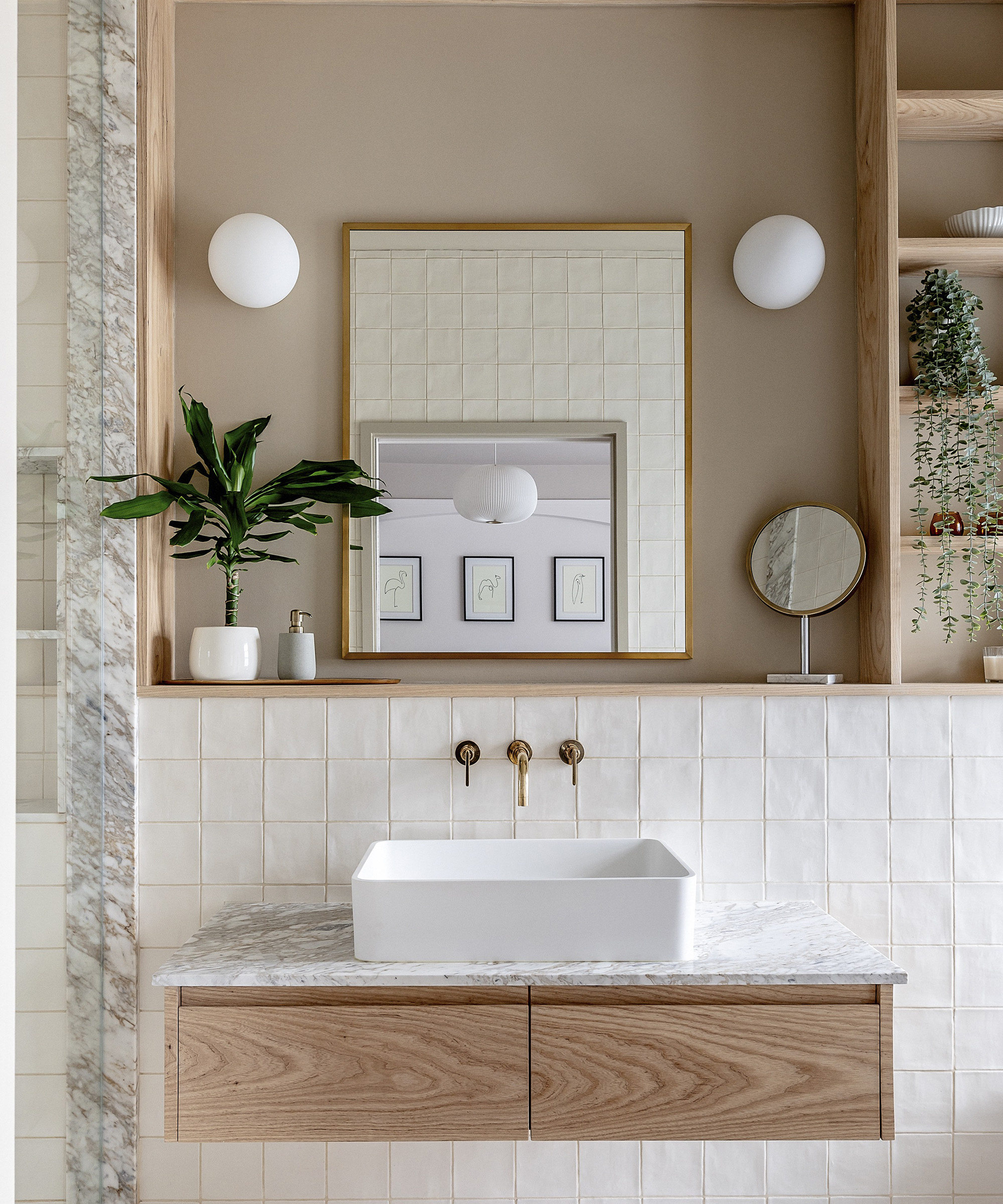 A newly fitted sink in a bathroom with soft brown walls and built in pine wood shelves. The splash back tiles are white and the taps are brass
