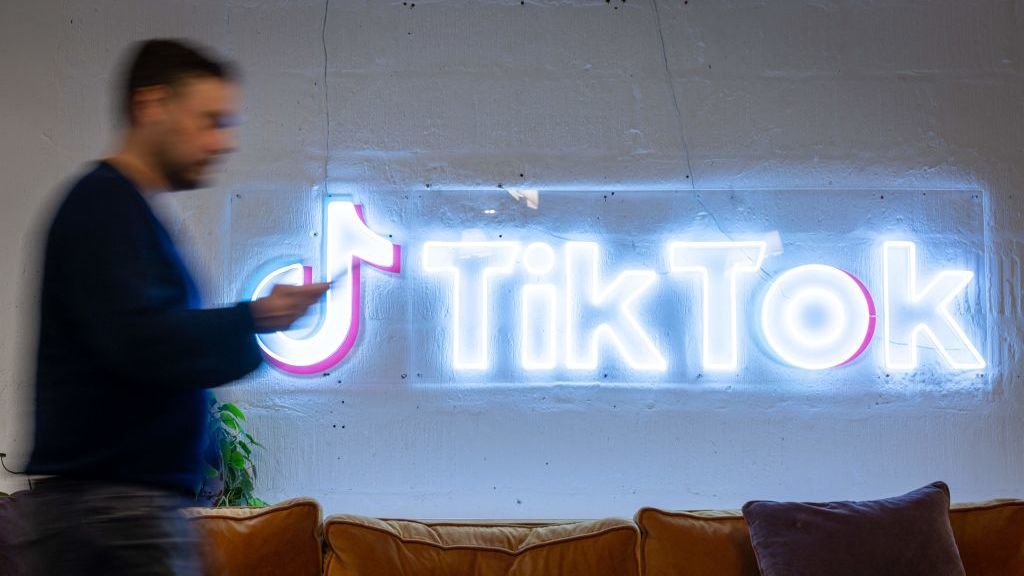 A man walking in front of a neon TikTok sign on an office wall