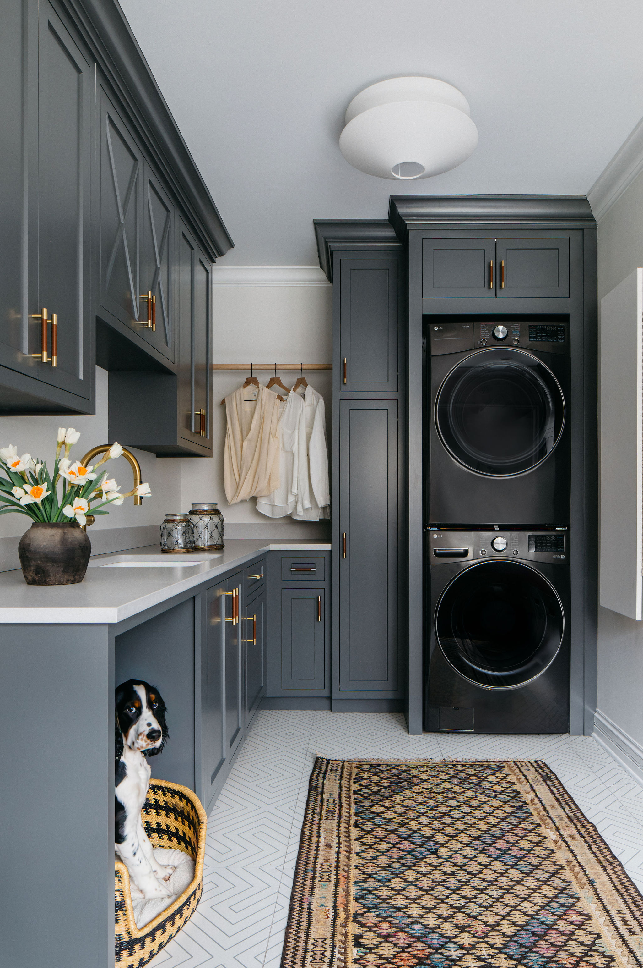 A utility room with dark gray cabinetry, a runner on the floor, and a wooden rail holding clothes