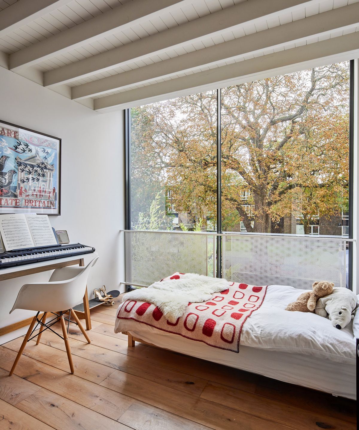A single bed and musical keyboard in a small teenage bedroom with large glazing and a bright bedspread