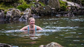 A woman wild swimming woman in clear mountain stream Lake District Cumbria