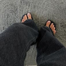 Person wearing black jeans with flip flops and neutral pedicure colour