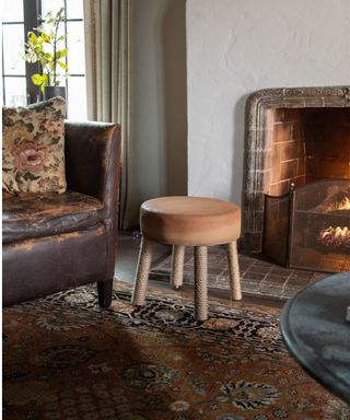 Brown ottoman stool with rope legs, leather armchair, patterned carpet by fireplace