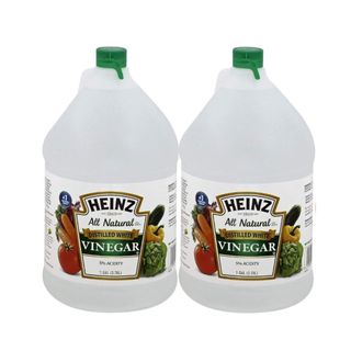 Two white bottles of vinegar with green and white labels that say 'Heinz' with dark green caps on the top