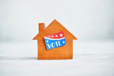 Small wooden house with a VOTE sticker in a bright white setting.