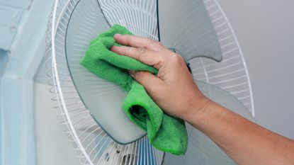 A hand cleaning a fan with a green cloth