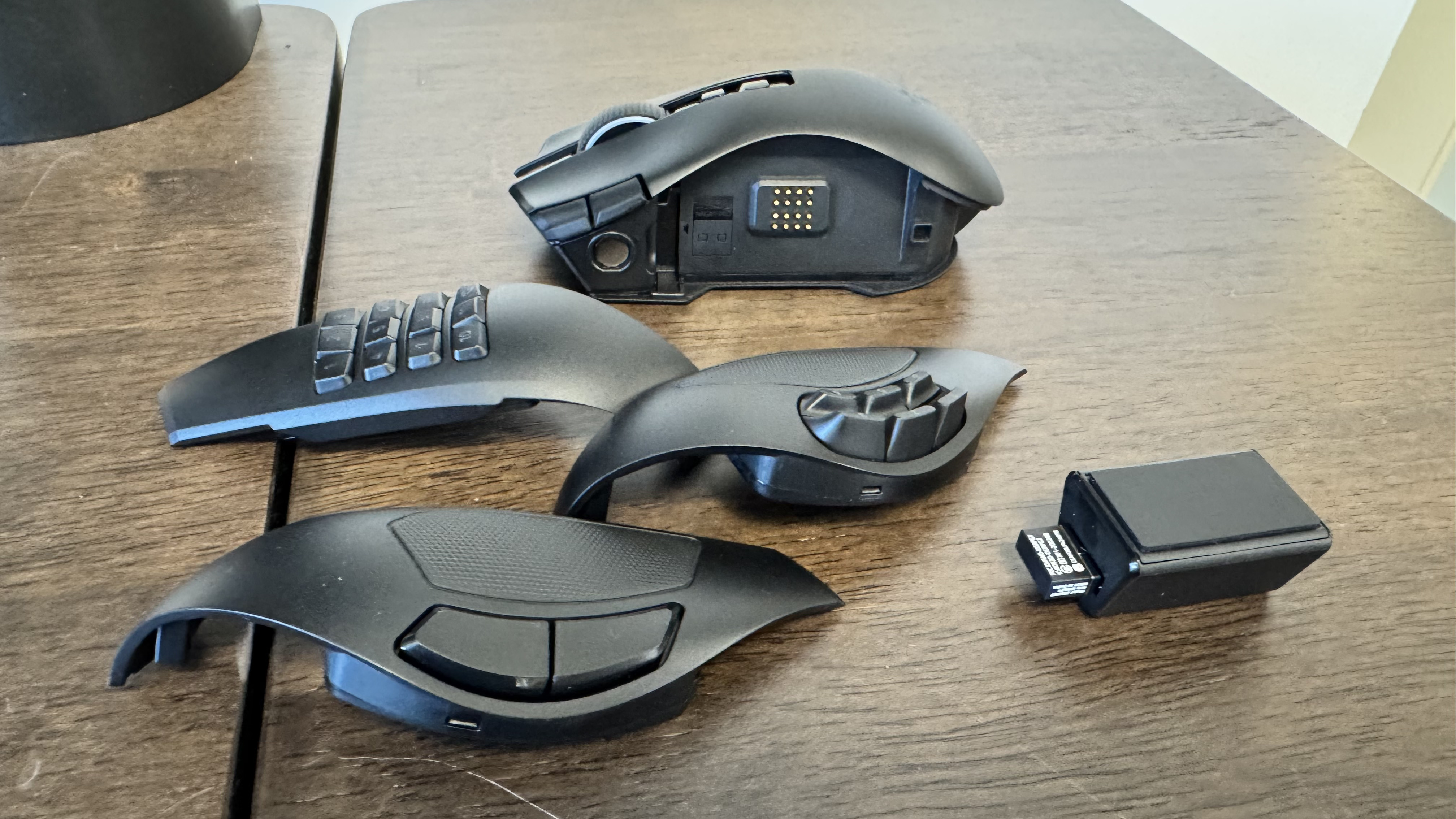 The Razer Naga V3 Pro, its three faceplate, and the connector on a wooden table
