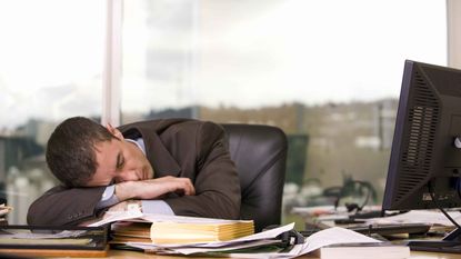 A businessman sleeps at his desk.