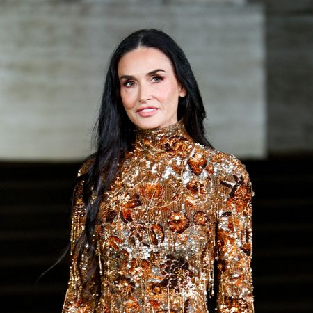a white woman with long dark hair wearing a long-sleeve gold gown with beads and sequins