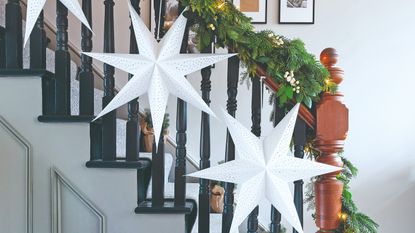 A hallway with a staircase with the railing decorated with a Christmas garland and star-shaped paper lanterns from IKEA