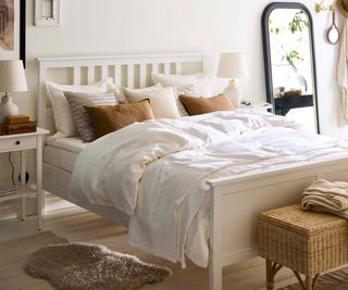 White sheets and brown and beige pillows on a white bed frame against a white wall.