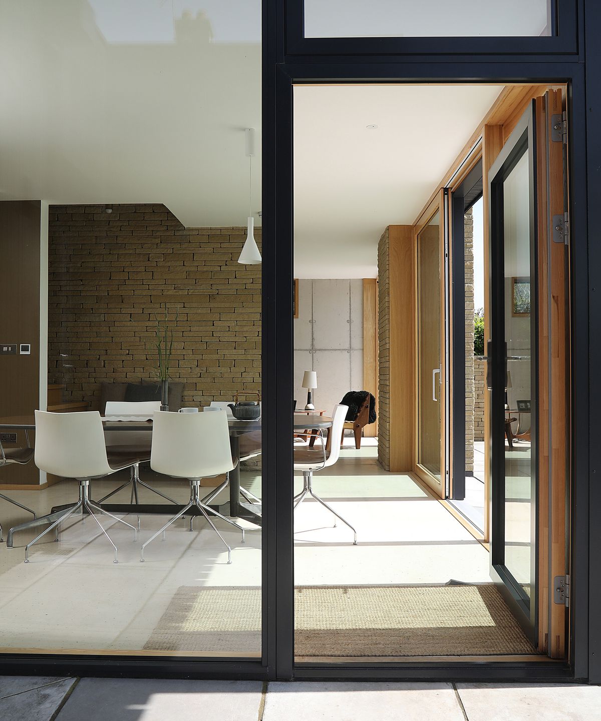 A glass wall with large door leading into a contemporary living space with minimalist interiors and pale floor