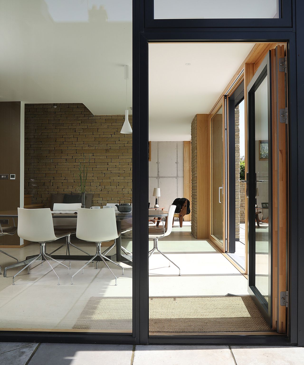 A glass wall with large door leading into a contemporary living space with minimalist interiors and pale floor