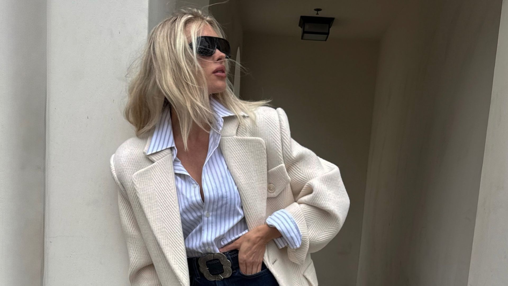 Elsa Hosk poses wearing dark wash cropped jeans with black loafers. She tucked a striped shirt into her jeans and layered a cream blazer on top.