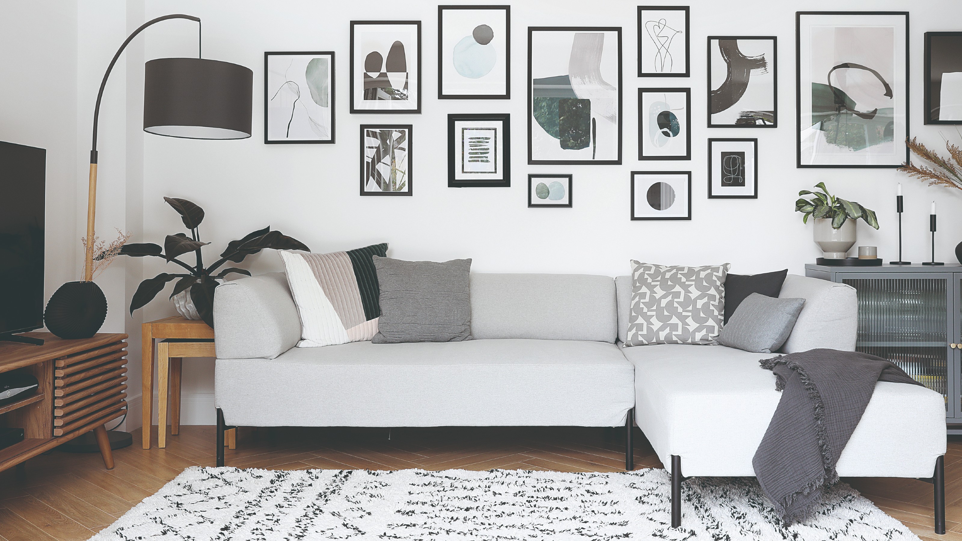 A living room with a chaise light grey sofa with metal legs and a gallery wall display