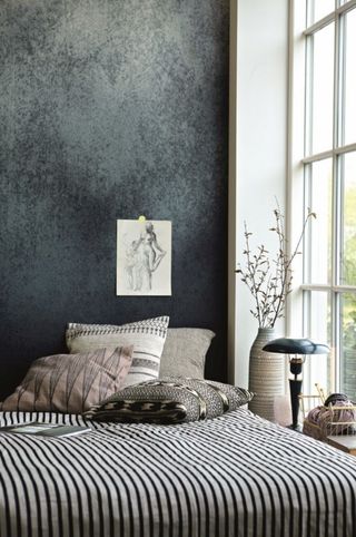 Dark distress wallpaper in bedroom with striped bed linen, mismatched decor and dried flowers