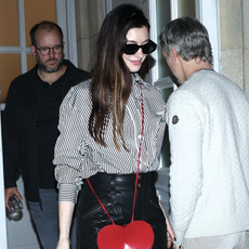 anne hathaway wears a striped button-up with leather pans and a red heart bag