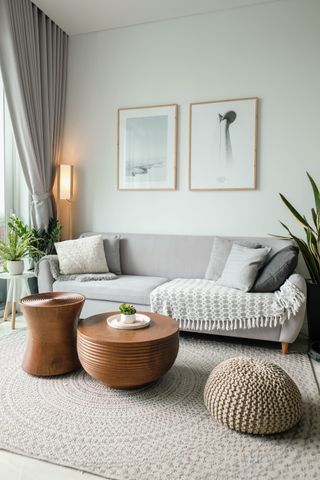 Cozy bright small living room with cream textured rug and light gray sofa with wooden abstract coffee tables and woven footstool