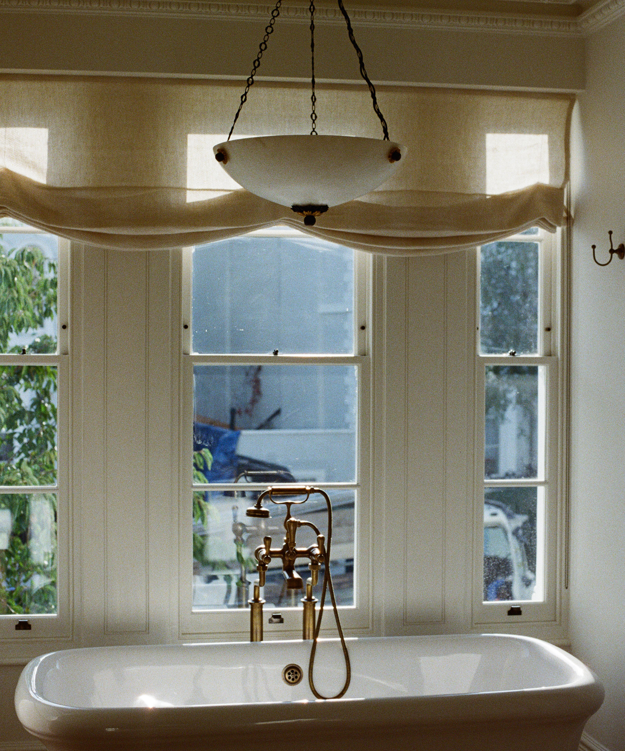 bath tub in a large window a with a sheer blind hanging across the top and a large pendant light above the bath
