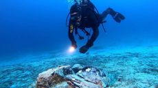 A scuba diver with a flashlight approaches a large piece of obsidian on the seafloor.