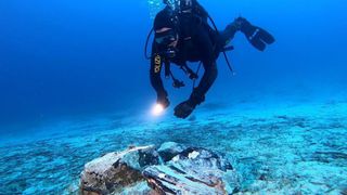 A scuba diver with a flashlight approaches a large piece of obsidian on the seafloor.