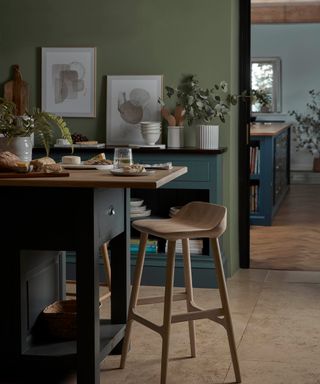 blue and green kitchen with small island with wooden bar stool