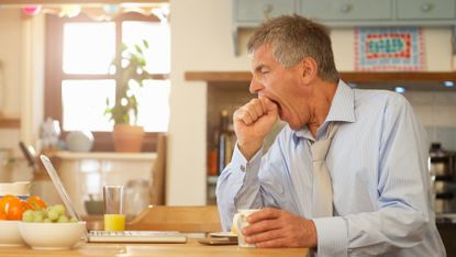 Tired man yawns at his breakfast table