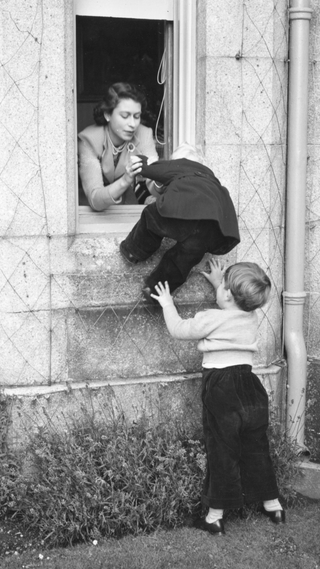 28th September 1952: Queen Elizabeth II and Charles, Prince of Wales helping Princess Anne through an open window at Balmoral Castle, Scotland