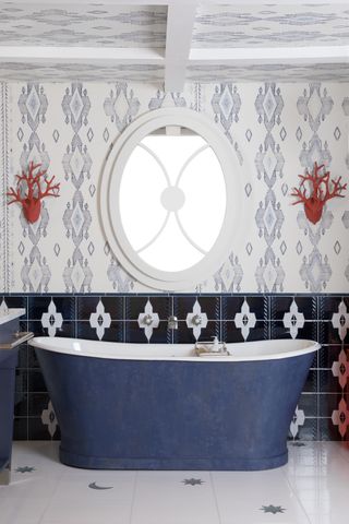 A navy blue free-standing bath on a white floor with star and moon motifs in front of a mirror and a wallpapered wall
