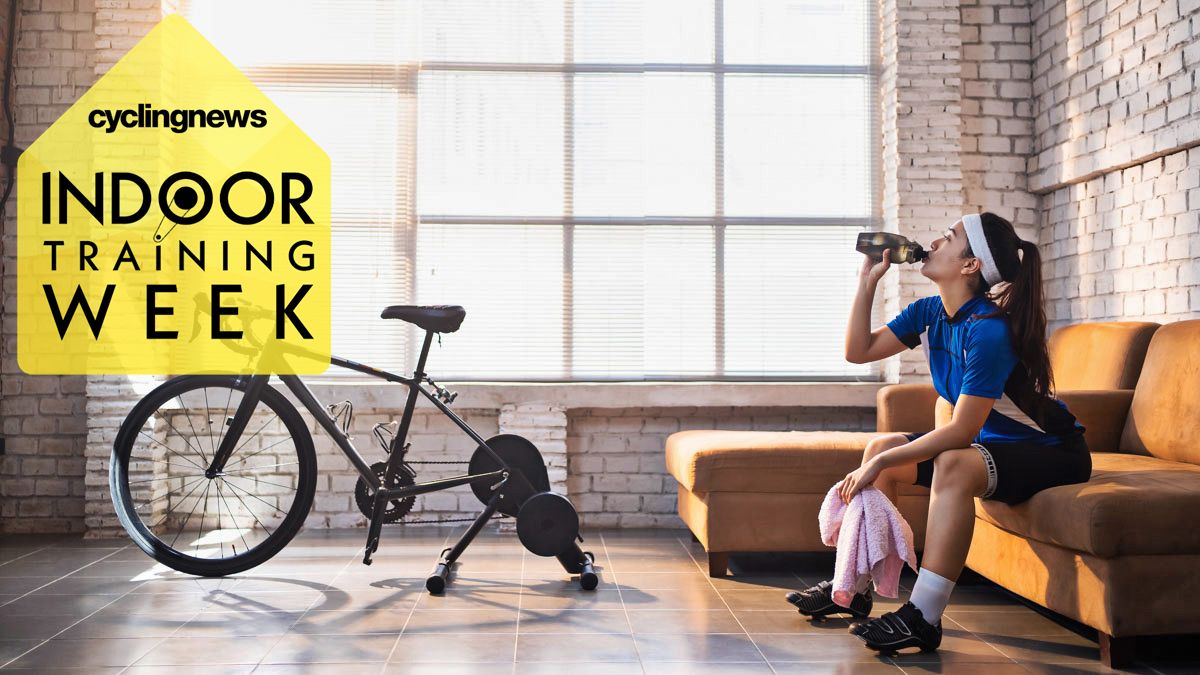 Woman sitting on a sofa drinking from a bottle of water, next to her turbo trainer with a yellow &#039;Indoor Training Week&#039; badge overlaid