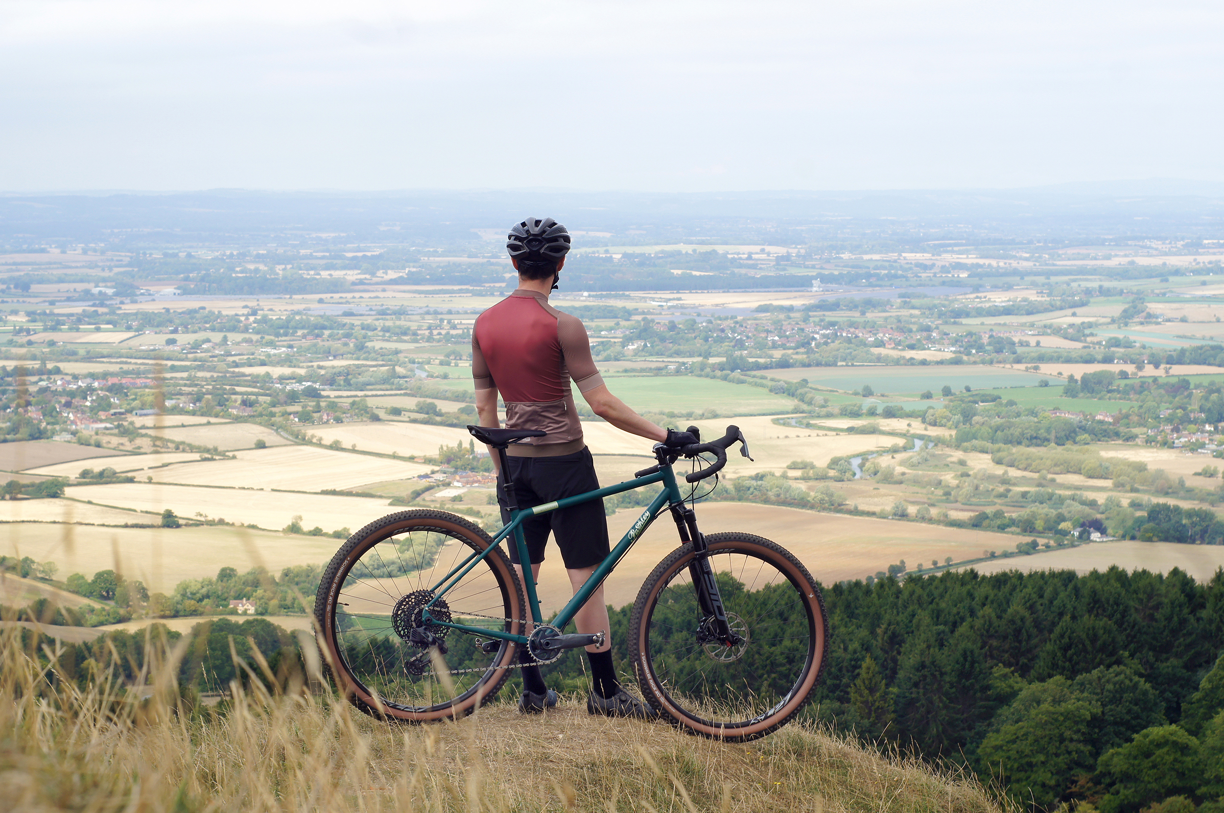 Man looking out over a sprawling green valley sitting with his gravel bike