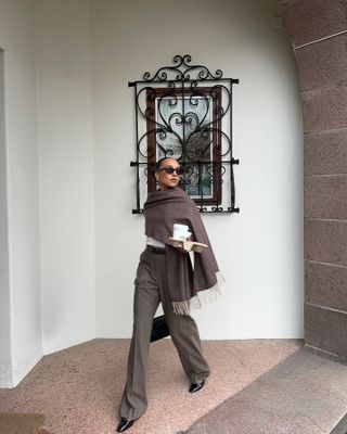 Ingrid wears a brown scarf, white top, brown pinstripe trousers, black flats, and black sunglasses.