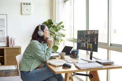 Woman wearing headphones working from home, sitting at desk in front of a monitor.