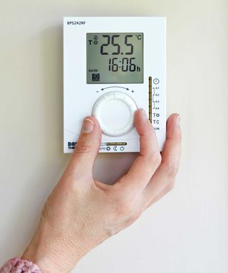 hand reaching for a thermostat set at 25 degrees celsius