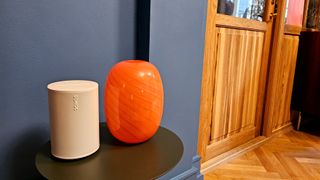 Hvid Sonos Era 100 på et bord med orange vase