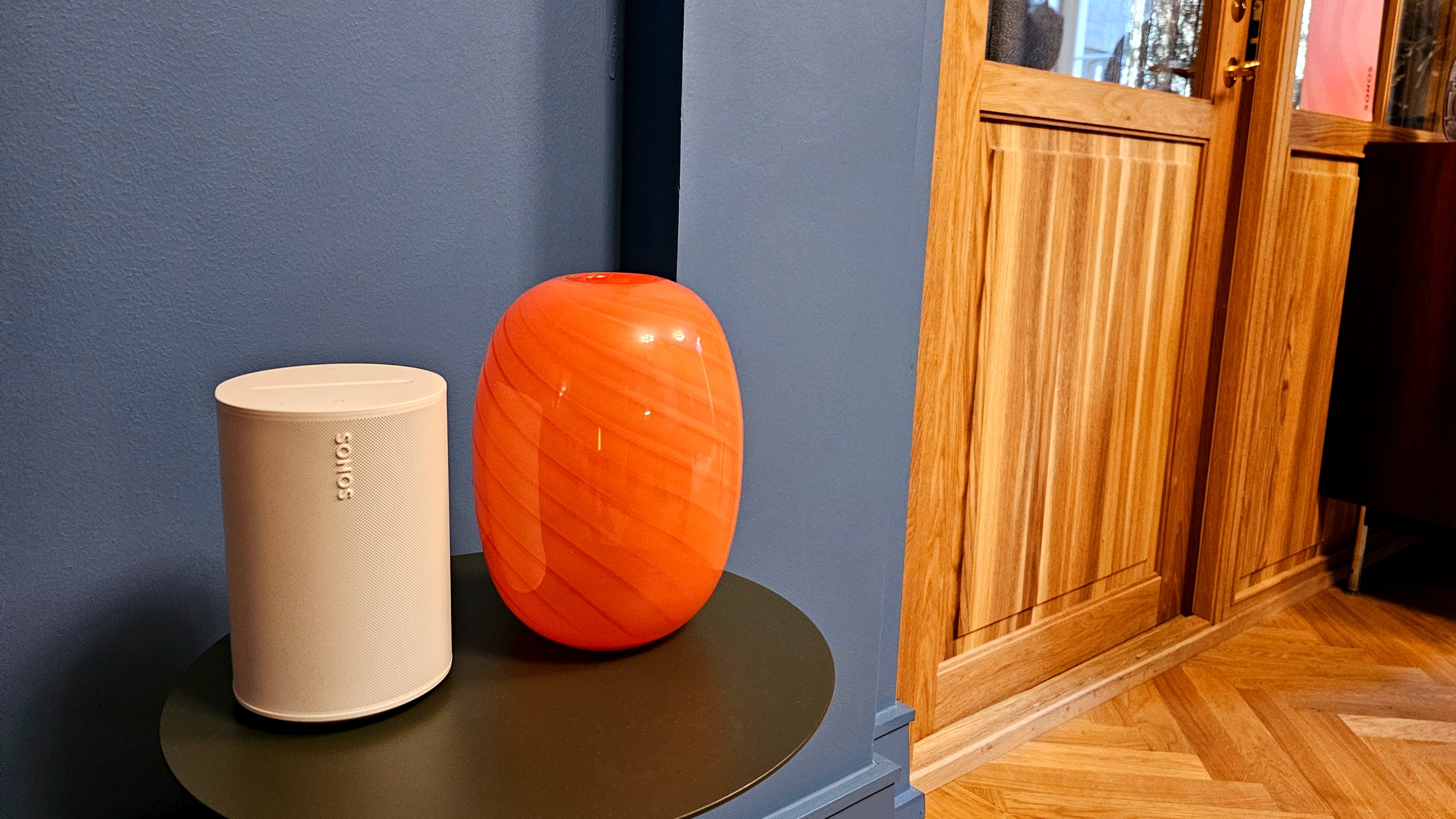 Hvid Sonos Era 100 på et bord med orange vase