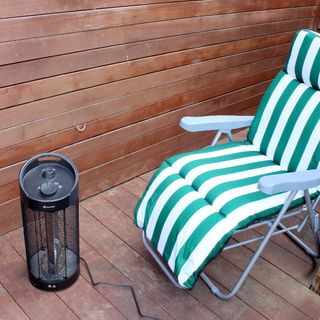 The Blumfeldt Heat Guru 360 patio heater being tested on wooden decking outdoors next to a green and white striped outdoor chair