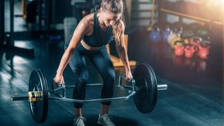 Woman performs trap bar deadlift in gym