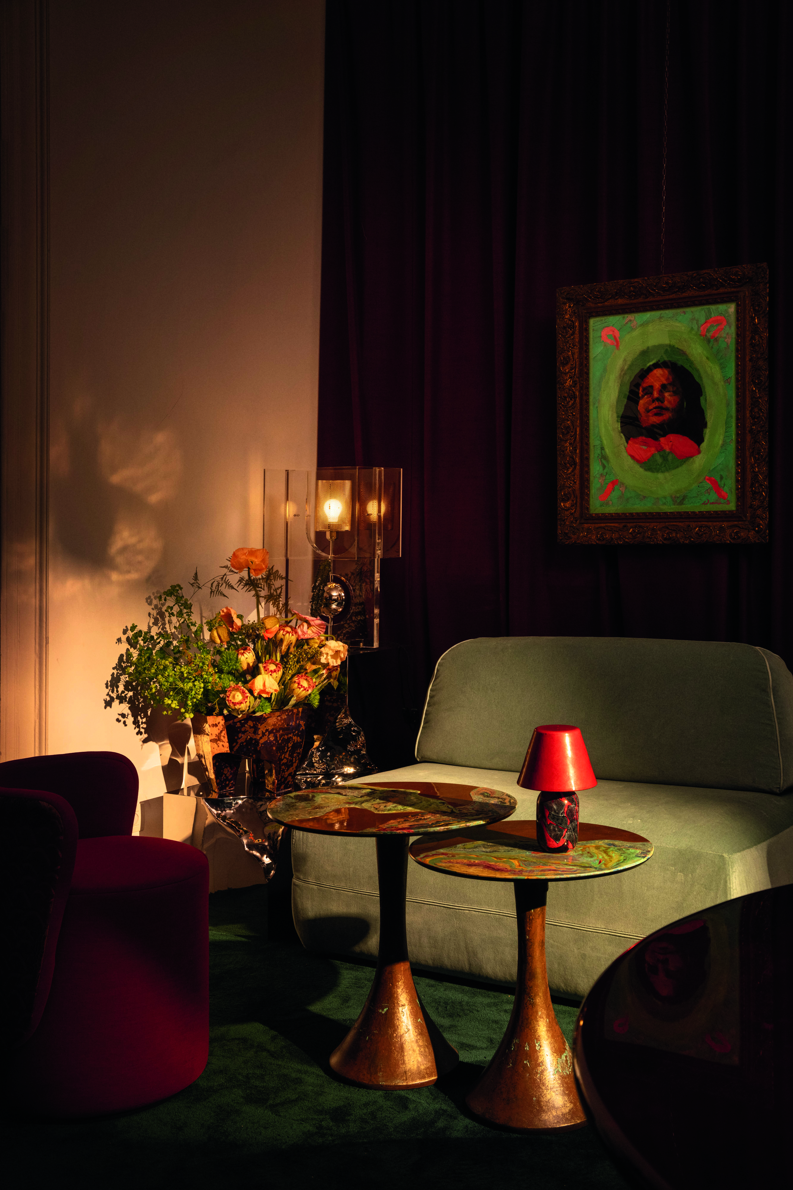 A sun-lit living room decorated with artisanal pieces in glass, wood, marbled copper, fresh flowers, plush, velvety seats, and a colorful artwork hanging on the wall.