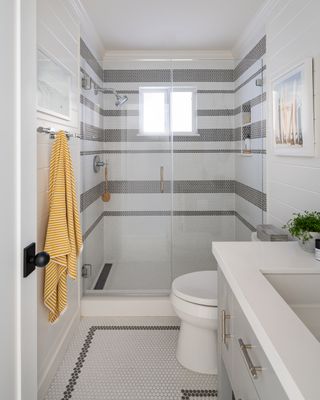 bathroom with shower, penny tiles on walls and floors, white scheme, vanity, glass doors