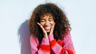 Portrait of laughing young woman with curly hair against white wall - stock photo
