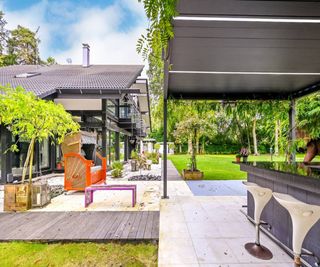 An outside bar and grill and swing chair on stone slabs around a grass garden