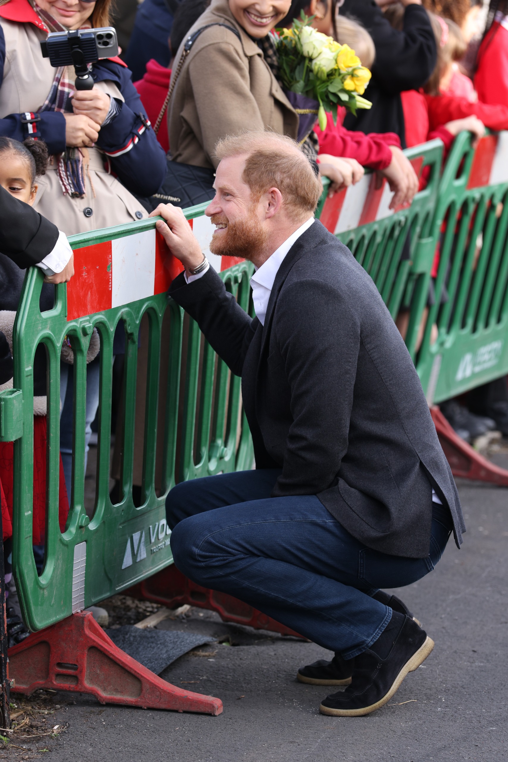 Prince Harry kneeling down leaning on a barrier