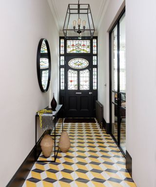 Bright hallway with bold yellow and black flooring, black metal console table, black metal and glass pendant light, baskets on the floor, black round mirror