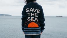 Finisterre Save The Sea jumper worn by model nea a large body of water