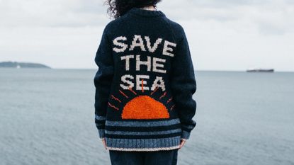Finisterre Save The Sea jumper worn by model nea a large body of water