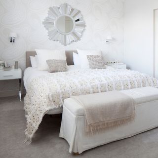 bedroom with white textured wall grey flooring and white bed with cushions