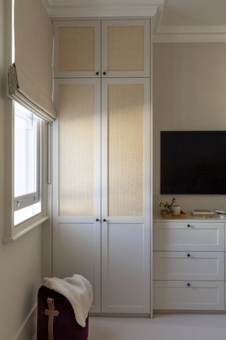 neutral bedroom with fitted wardrobe, chest of drawers, TV mounted on wall, cream blinds at window